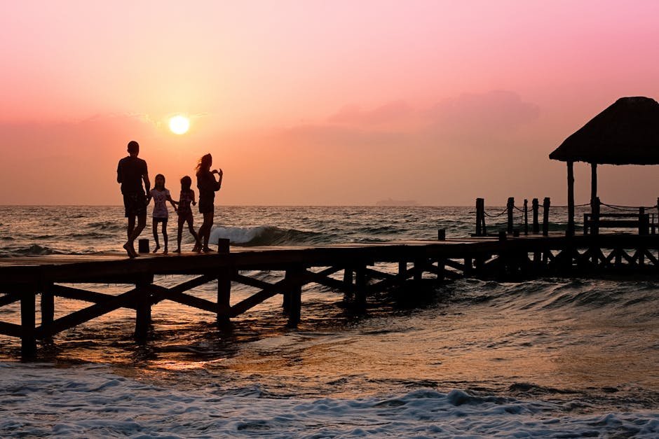 Silhouetted family enjoys a stroll on the beach pier at a vibrant sunset over the ocean waves.