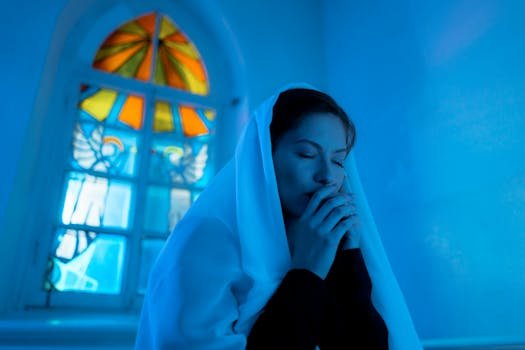 A woman prays quietly in a chapel with vibrant stained glass, capturing a serene moment of worship.