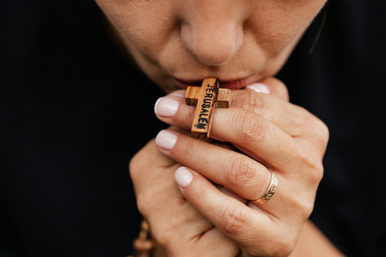 A close-up image of a person holding and kissing a wooden cross rosary in prayer.