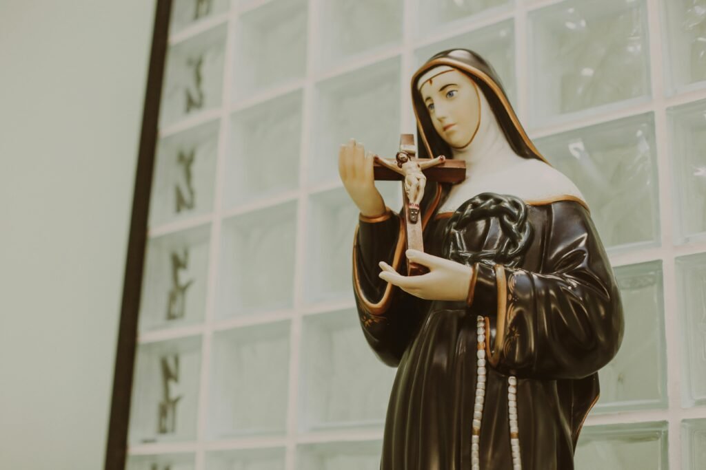 Statue of religious saint holding crucifix indoors, symbolizing faith and devotion.