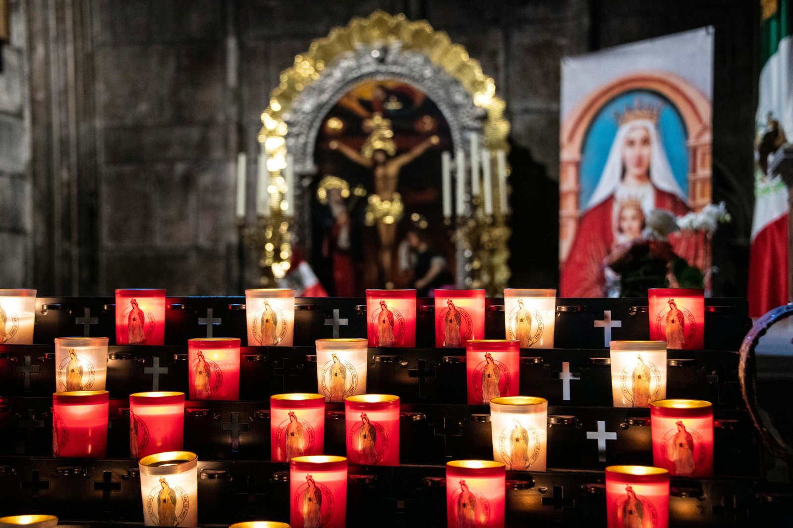 Votive candles illuminate a sacred altar in a Parisian church with religious icons and cross symbols.