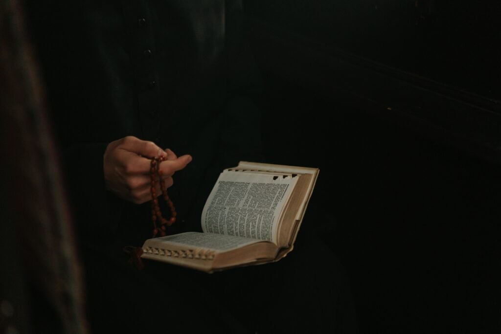 A priest holds a rosary and open Bible, symbolizing faith and devotion.