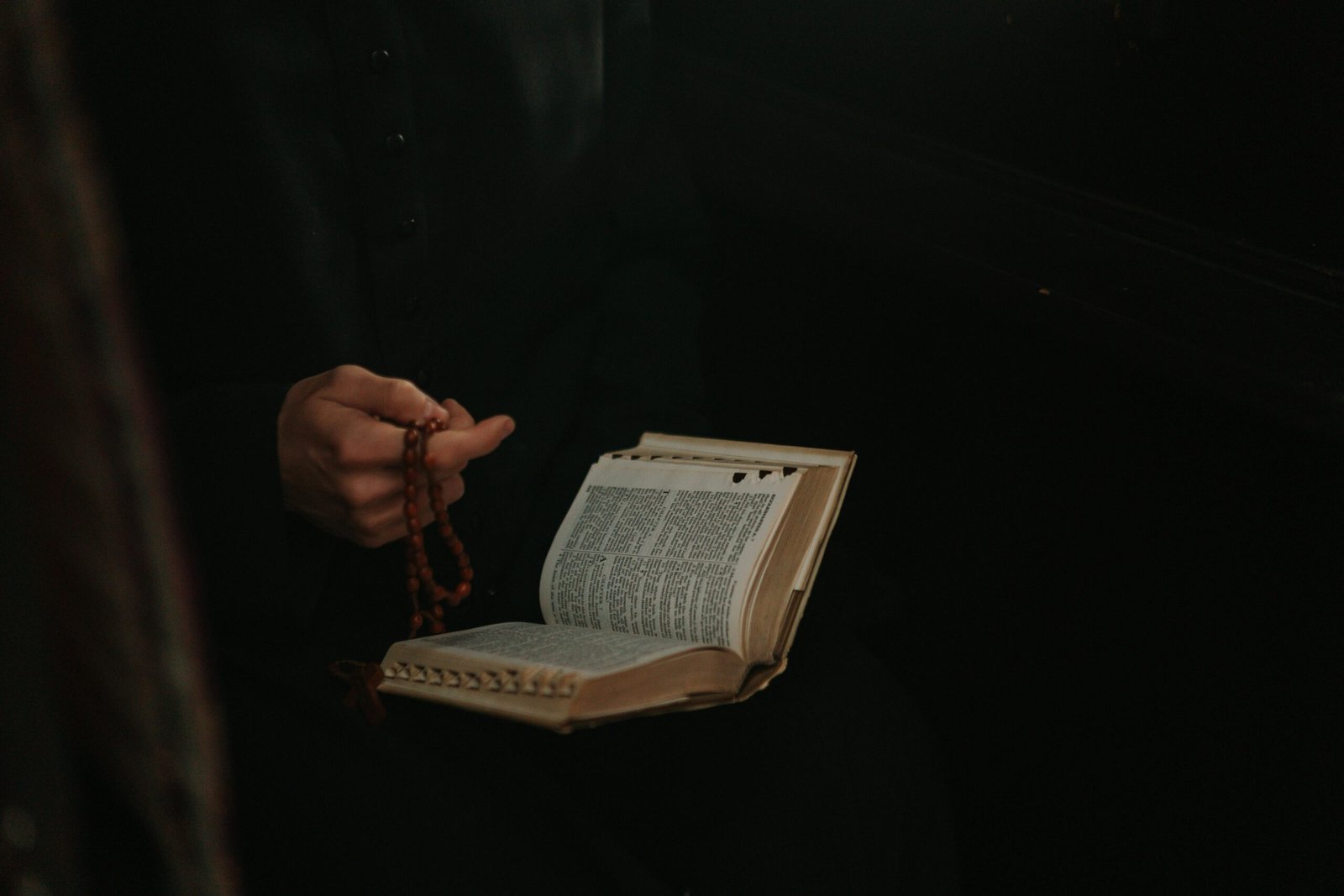 A priest holds a rosary and open Bible, symbolizing faith and devotion.