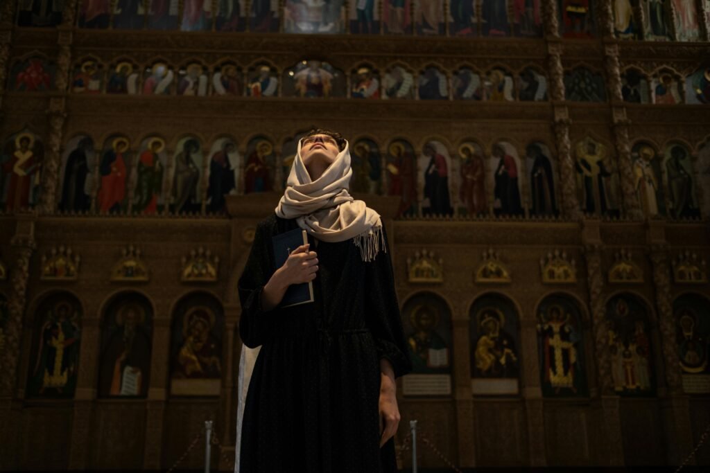 A woman with a headscarf looks up inside a church, holding a book.