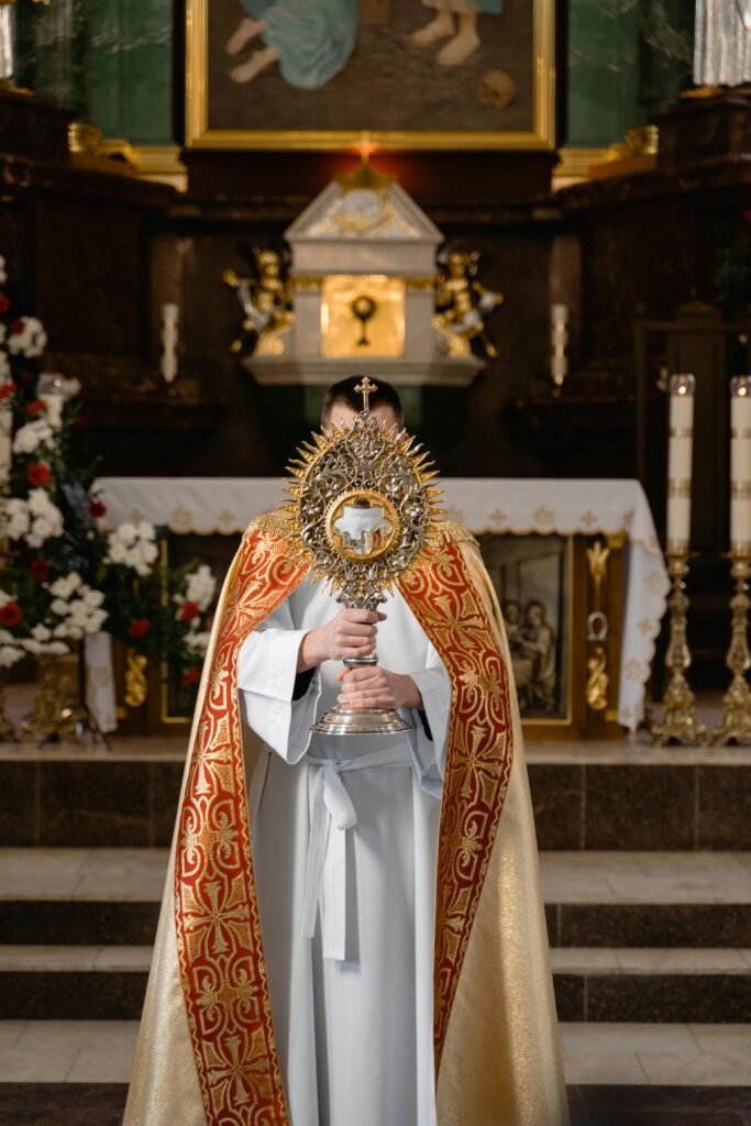 A priest in vestments holds a monstrance in front of a church altar, emphasizing solemn devotion.