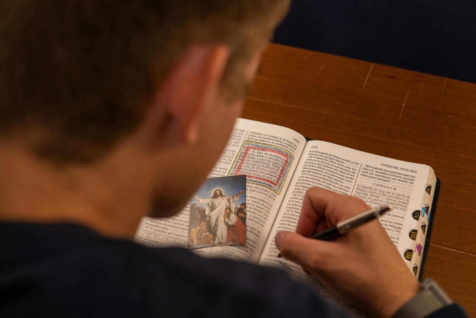 A person makes notes while reading a Bible with a photo of Jesus, focusing on study and faith.
